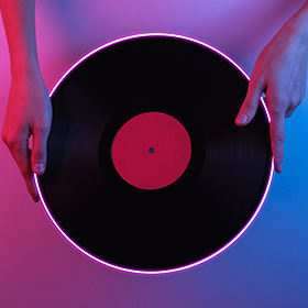 レコードをネオンが輝く背景の中で人が両手で持っている画像